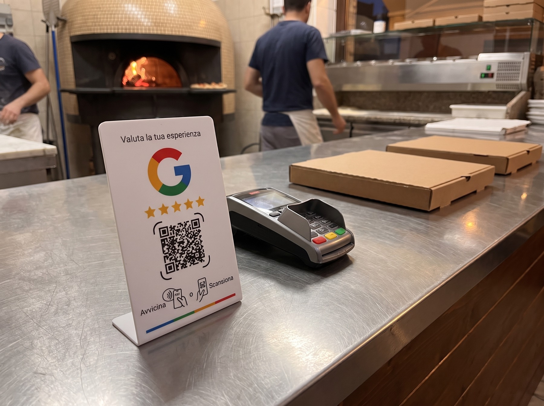 Espositore autoportante per recensioni Google sul banco ritiro di una pizzeria d'asporto, accanto al POS